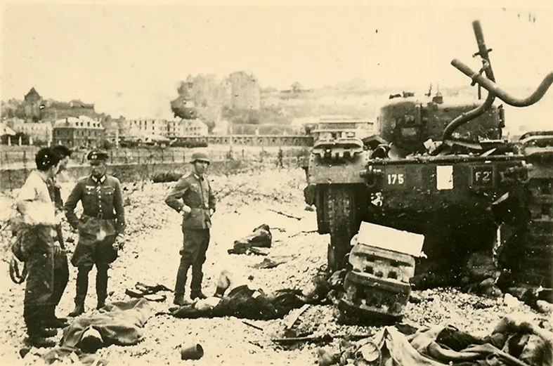 Sur la plage de galets de Dieppe, soldats allemands et victimes canadiennes devant un char détruit.