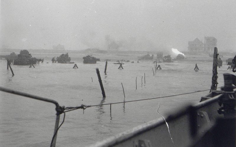 Vue prise depuis le LCT 610. Sword Beach, secteur Queen Red, vers 8h00. Un char du 22e Dragon brule après avoir été touché par un tir allemand.