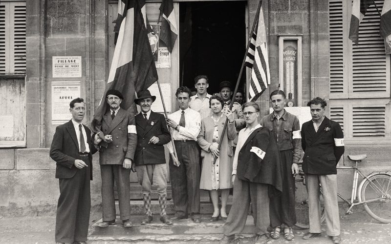 4 juillet 1944.Le jour de la fête nationale américaine, des habitants de Trévières posent avec des drapeaux français et américain.