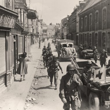 Des ambulances passent entre des soldats américains, dans une rue de Carentan.