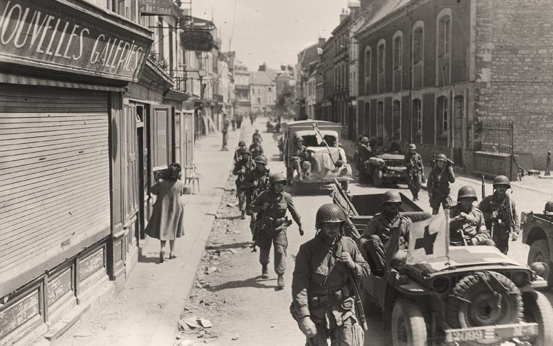 Des ambulances passent entre des soldats américains, dans une rue de Carentan.